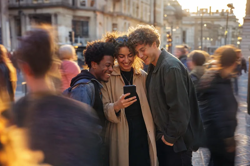 Friends laughing over a phone on a busy street